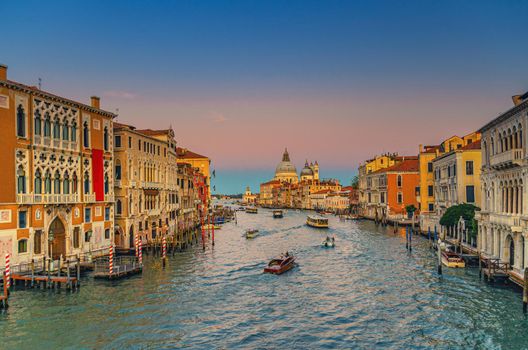 Venice cityscape with Grand Canal waterway. Buildings with evening lights along Grand Canal. Santa Maria della Salute Roman Catholic church on Punta della Dogana at twilight. Veneto Region, Italy.