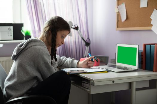 Green screen on laptop. At home in her room, a teenager sits at her desk solving assignments from school. A diligent student. Remote learning at home.