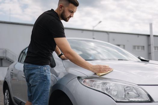 Hand of man wipes headlight of his car using rug. Self-service car wash. Outdoor.