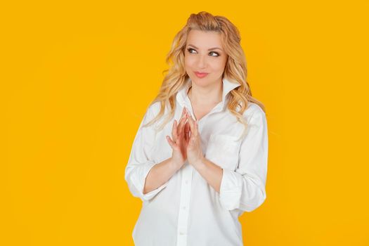 A blonde European woman in a white shirt, as if making a plan in mind, smiling mysteriously, looking to the side, wanting to do something illegal or secretly. I have a great idea. yellow background