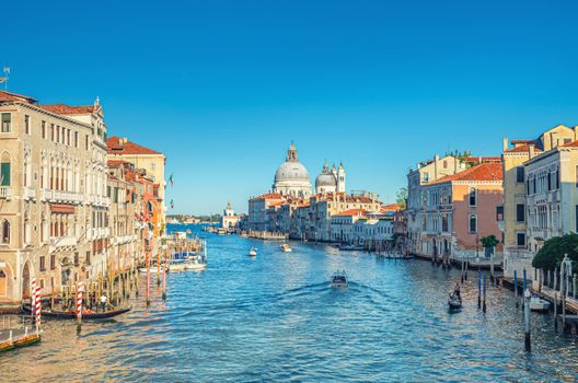 Venice cityscape with Grand Canal waterway. Gondolas and boats docked and sailing Canal Grande. Santa Maria della Salute Roman Catholic church on Punta della Dogana. Veneto Region, Italy.