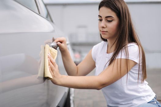 Front view of attractive happy joyful female driver washing her car with special rag in self-service car wash.