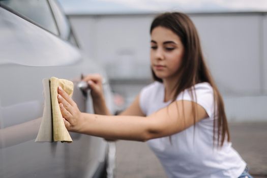 Attractive happy joyful female driver wipe her car using rag in self-service car wash. Focus on hand.