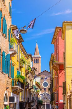 Typical italian street with traditional colorful buildings, shutter windows and balconies with plants, tower Campanile di Santa Anastasia church, Verona city historical centre, Veneto Region, Italy