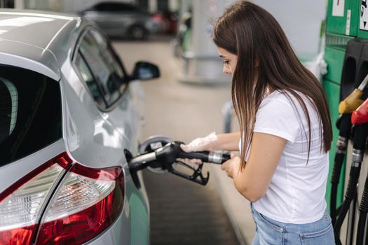 Attractive young woman refueling car at gas station. Female filling diesel at gasoline fuel in car using a fuel nozzle. Petrol concept. Side view.