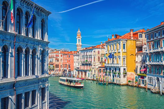 Grand Canal waterway in Venice historical city centre with vaporetto, Venetian architecture colorful buildings and Church of the Holy Apostles of Christ bell tower. Veneto Region, Northern Italy.