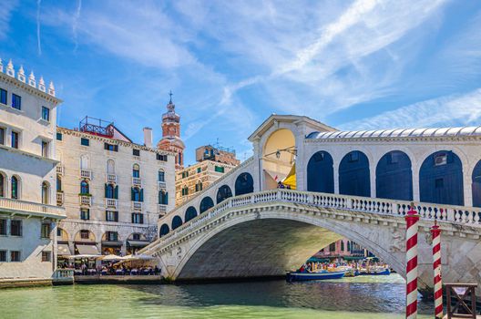 Venice cityscape with Rialto Bridge across Grand Canal waterway, Venetian architecture colorful buildings, blue sky in sunny summer day. Veneto Region, Northern Italy.