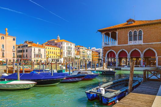 Boats moored in wooden pier dock of Grand Canal waterway in Venice historical city centre with Rialto Mercato, row of colorful buildings Venetian architecture. Veneto Region, Northern Italy.