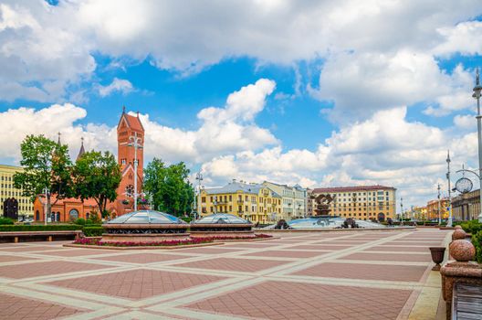 Independence Square in Minsk city centre with Saints Simon and Helena Roman Catholic church or Red Church and Minsk Hotel building, blue sky white clouds in sunny summer day, Republic of Belarus