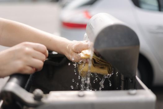 Female wash rug in water. Close-up woman's hand in front of car on self servise car wash. Squeez rug.