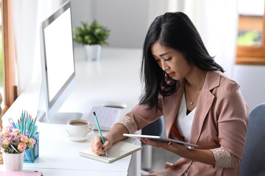 Business woman entrepreneur using digital tablet and making notes on notebook.