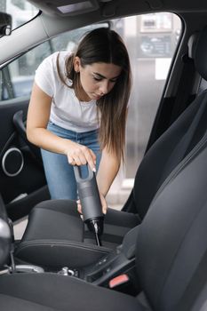 Female using portable vacuum cleaner in her car. Electrical vacuum in woman's hand clean car inside from dust. Self servise car wash.