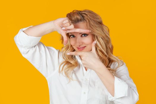 A blonde in a white shirt, middle aged European woman, a designer creating a new project, looks at the footage and smiles, and stands against a yellow background to create the perfect shot