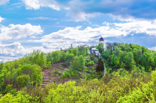 Diana Observation Tower Rozhledna Diana and funicular on hill above Slavkov Forest with green trees and Karlovy Vary Carlsbad town, blue sky white clouds background, West Bohemia, Czech Republic