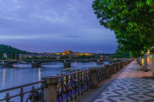 Prague with promenade riverside road, Prague Castle, St. Vitus Cathedral in Hradcany district, bridges over Vltava river, night evening twilight view, Bohemia, Czech Republic