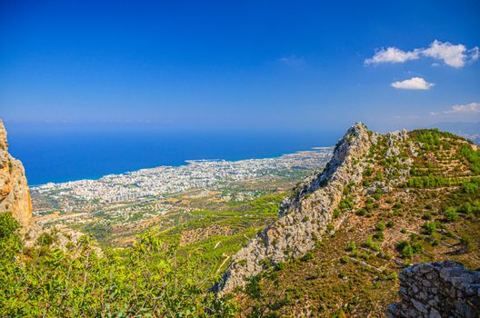 Aerial view of Kyrenia Girne mountain range and valley in front of Mediterranean sea, green trees on rock foreground, blue sky in sunny day, Northern Cyprus