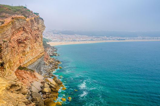 Aerial view of rocks and cliffs, azure turquoise water of Atlantic Ocean and sandy beach coastline Praia da Nazare town, Leiria District, Oeste region, Portugal