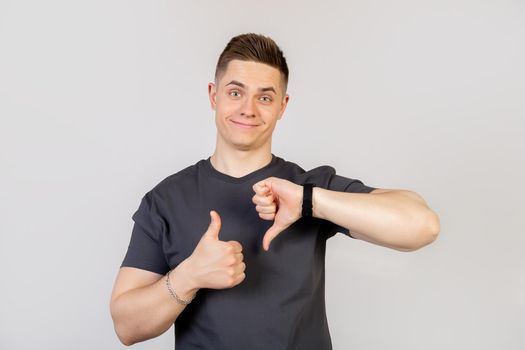 The guy shows a finger up and down gesture. Young handsome man on an isolated background. Do thumbs up and down, disagreement and expression of agreement. Crazy conflict