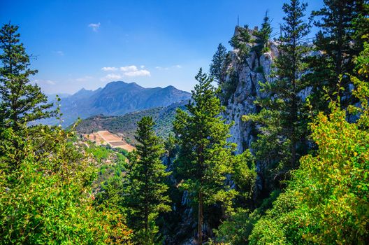 Kyrenia Girne mountain range from medieval Saint Hilarion Castle with green trees and rocks, blue sky white clouds in sunny day, Northern Cyprus