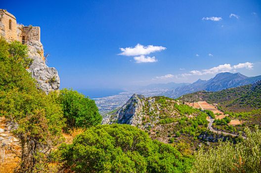 Aerial view of Kyrenia Girne mountain range and valley in front of Mediterranean sea, green trees on rock and ruins of Saint Hilarion Castle foreground, blue sky in sunny day, Northern Cyprus