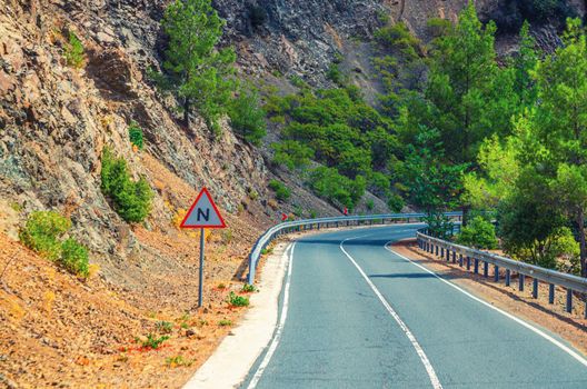 Asphalt serpentine road in Troodos mountain range with roadside fence and trees, Cyprus