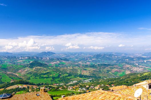 Aerial top panoramic view of landscape with valley, green hills, fields and villages of Republic San Marino suburban district with blue sky white clouds background. View from San Marino fortress