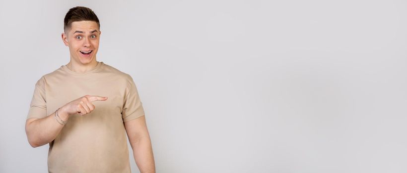 Handsome strong young man pointing finger to the right with a surprised expression on his face. Copy ad space