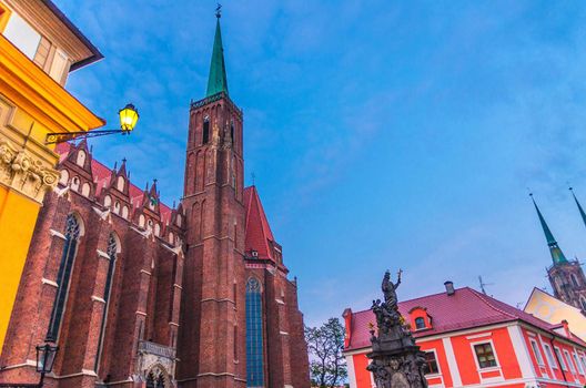 Monument and street light on square and Collegiate catholic Church of Holy Cross and St. Bartholomew building with spire in old historical city centre Ostrow Tumski, evening view, Wroclaw, Poland