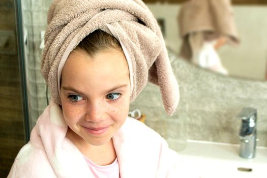 Relaxed young girl model wears towel wrapped on head, feels refreshed after taking shower, has healthy clean soft skin, poses in cozy bathroom. Girl, beauty and hygiene concept. High quality photo