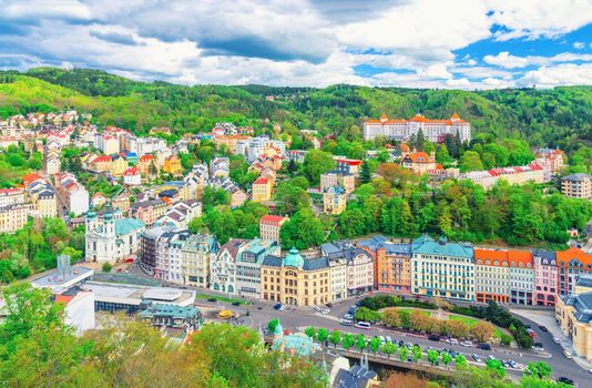 Karlovy Vary Carlsbad historical city centre top aerial view with colorful beautiful buildings, Slavkov Forest hills with green trees, blue sky white clouds background, West Bohemia, Czech Republic