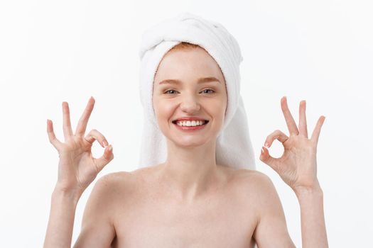 Beauty treatment. Woman applying moisturizing cream skin care product on face, making ok sign studio shot.