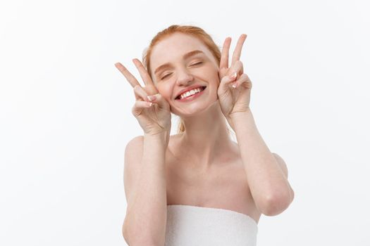 Close-up of beautiful young woman with bath towel covering her breasts, on gray, shows two fingers sign