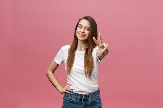 Portrait of a cheerful trendy woman showing two fingers sign over pink background.