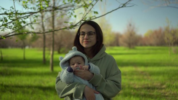 A young mother walks with a baby in nature. A girl with glasses holds a child in her arms. Closeup. 4k