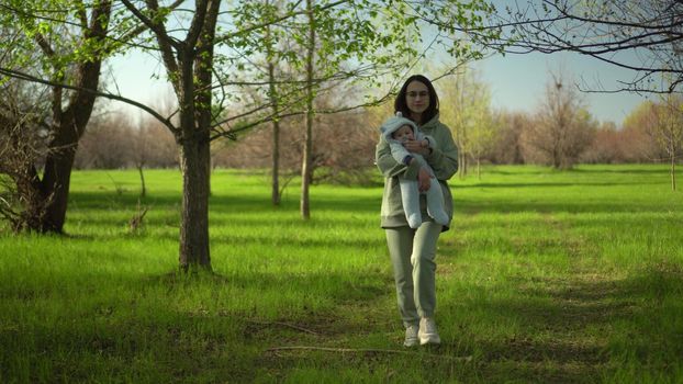 A young mother walks with a baby in nature. A girl with glasses holds a child in her arms. 4k