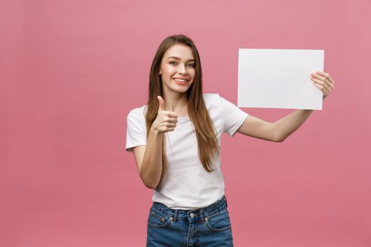 Young beauty woman hold blank card and showing thumbs up over pink background.