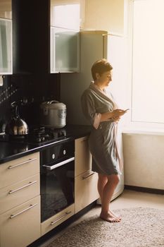 Work from home. Pretty woman in a bathrobe in the kitchen in the morning communications and works on the phone at home. Working at home