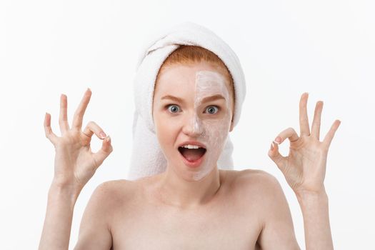 Beauty treatment. Woman applying moisturizing cream skin care product on face, making ok sign studio shot.