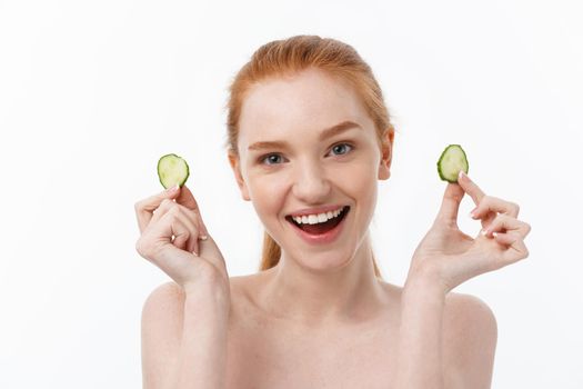 Close up beauty portrait of a smiling beautiful half naked woman holding cucumber slices at her face isolated over white background.