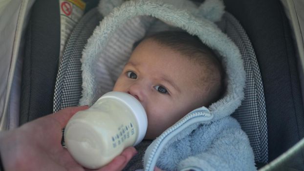 A baby in a stroller sucks milk from a bottle. A newborn baby eats on a walk close-up. 4k