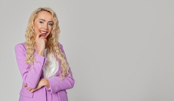 Attractive charismatic blonde woman with blue eyes laughing joyfully biting her finger, smiling contented, winning a university exchange program, smiling happily on a white background