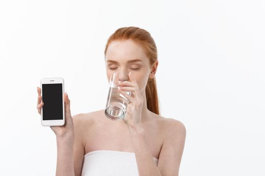 Happy smiling young woman with healthy skin reading and writing in mobile phone sms and drinking clean water. Consulting the diet. Closeup portrait.