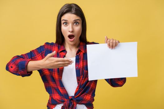Amazement or surprised female with blank white panel, isolated on yellow background