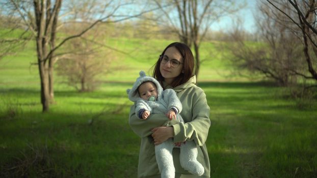 A young mother walks with a baby in nature. A girl with glasses holds a child in her arms. Closeup. 4k