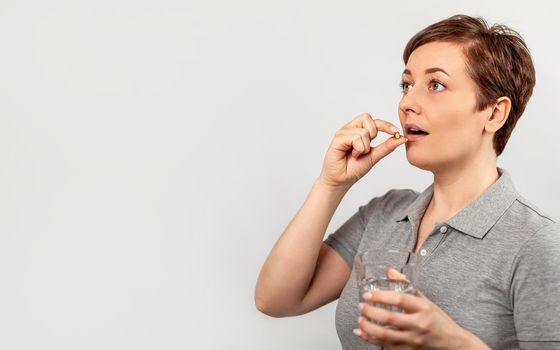 Woman holding a pill and a glass of water. The concept of daily medication, multivitamins and nutritional supplements, medications for the treatment of headaches, painkillers, and abdominal pain.