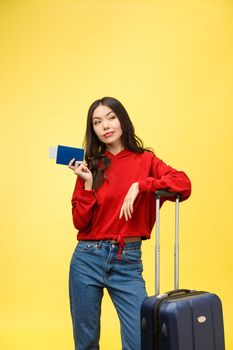 Woman travel. Young beautiful asian woman traveler with suitcase and passport on yellow background.