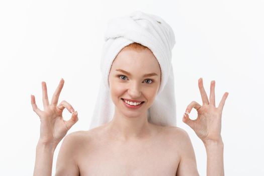 Beauty treatment. Woman applying moisturizing cream skin care product on face, making ok sign studio shot.