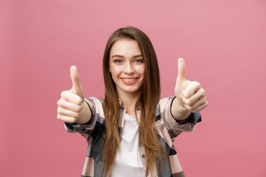 Close-up shot of smiling pretty girl showing thumb up gesture. Female isolated over pink background in the studio