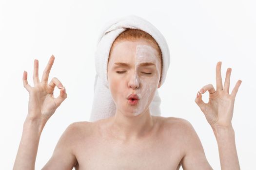 Beauty treatment. Woman applying moisturizing cream skin care product on face, making ok sign studio shot.