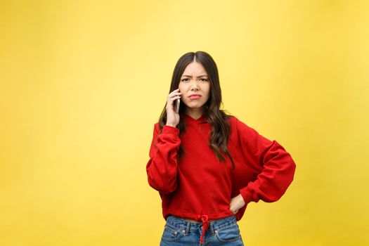 Portrait angry young asian woman disappoint at mobile phone while standing over yellow background.